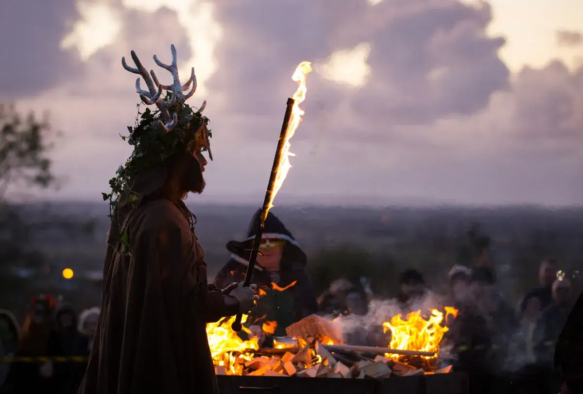 Mann mit Geweih-Kopfschmuck hält brennende Fackel. Ein Feuer brennt. Die Ursprünge von Halloween liegen in Irland.