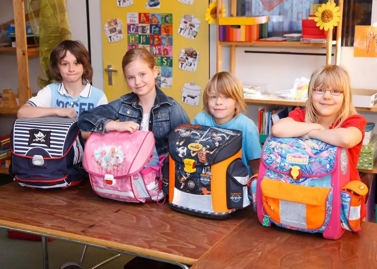 Vier Kinder der ersten Klasse Grundschule posieren stolz mit ihren neuen, bunten Schultaschen.