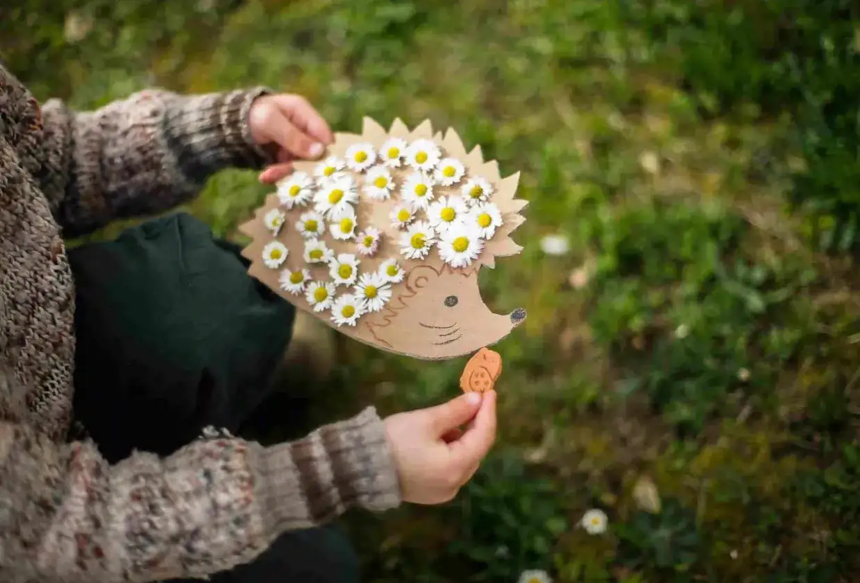 Ein Kind h&auml;lt einen Igel aus Pappe, verziert mit G&auml;nsebl&uuml;mchen. Ein tolles Bastelprojekt f&uuml;r den Kindergarten!