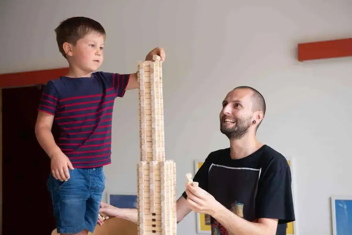 Ein Junge und ein Mann bauen mit Holzst&auml;bchen einen hohen Turm. Kreatives Bauen mit Alltagsmaterialien im Kindergarten f&ouml;rdert Fantasie und Teamwork.
