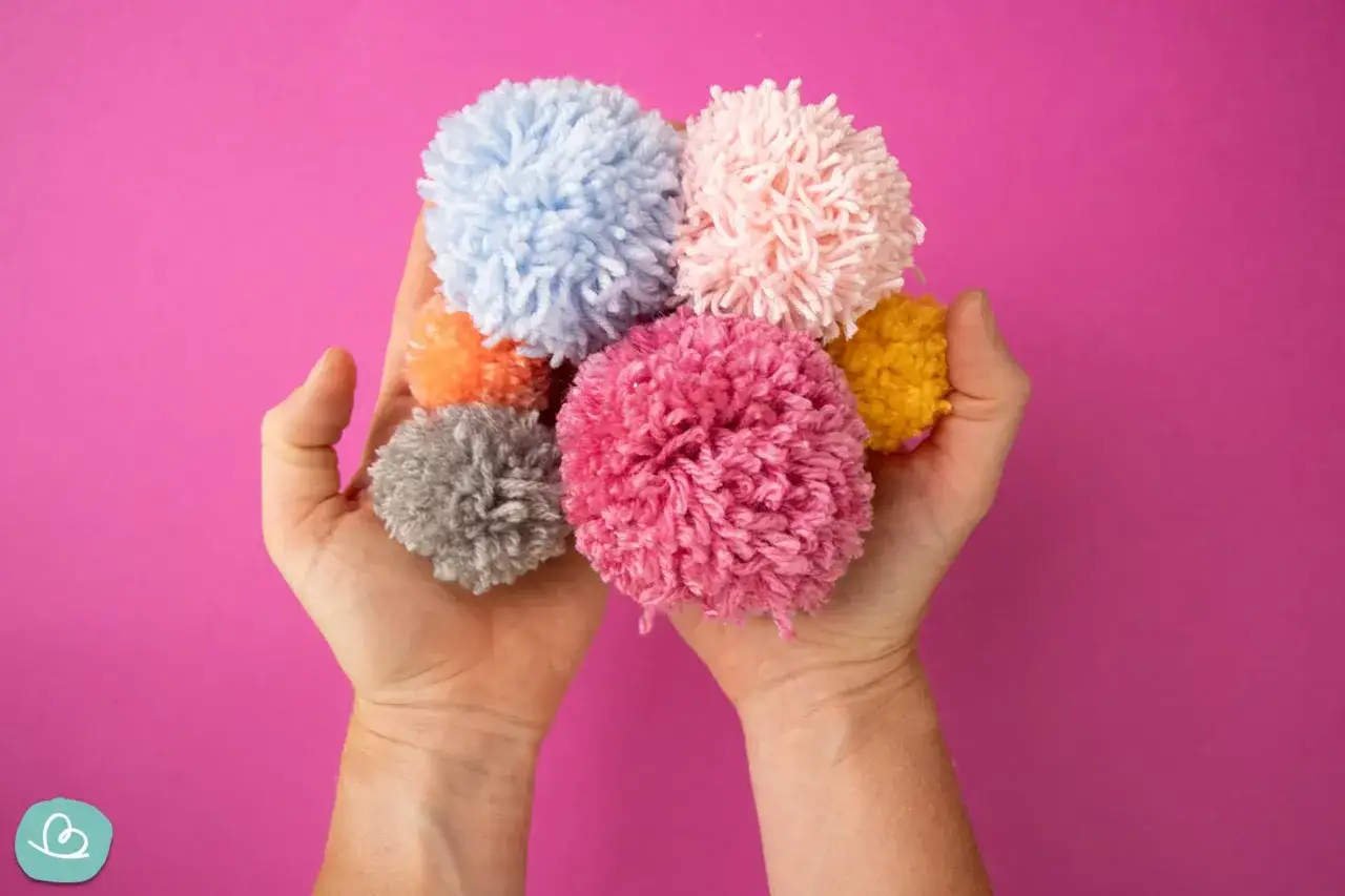 H&auml;nde halten bunte Pompons, die zum Pompons basteln einladen.
