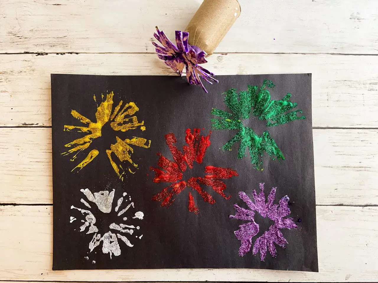 Buntes Silvester basteln mit Kindern: Glitzernde Feuerwerke in Gold, Rot, Gr&uuml;n, Silber und Lila auf schwarzem Papier, gestempelt mit einer Klopapierrolle.