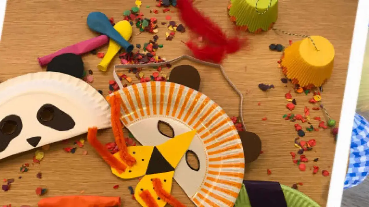 Basteln f&uuml;r Fasching: Papierplatten-Masken von Panda und L&ouml;we, bunte Federn und Konfetti liegen bereit.