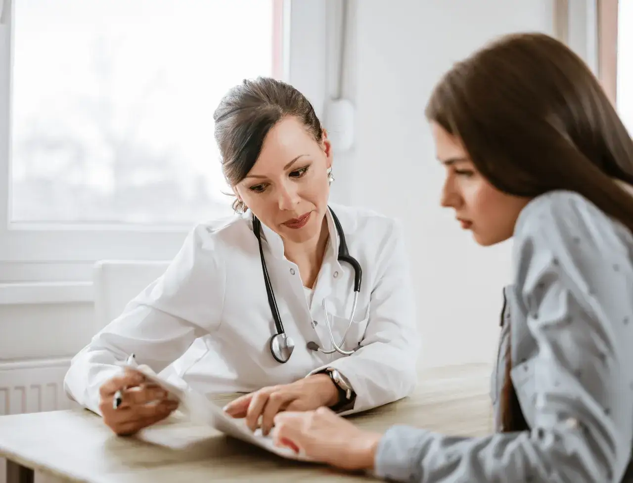 Ärztin erklärt Patientin, wie finde ich heraus ob ich ADHS habe. Sie besprechen Unterlagen am Tisch.