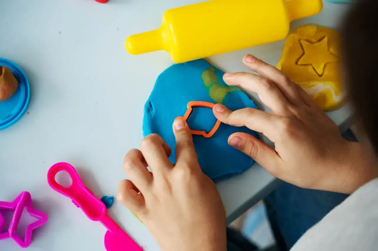 Kinderh&auml;nde formen bunte Knete. Ein gelber Nudelholz und Stern-Ausstecher liegen bereit. Perfekt f&uuml;r Fingerspiele im Kindergarten.