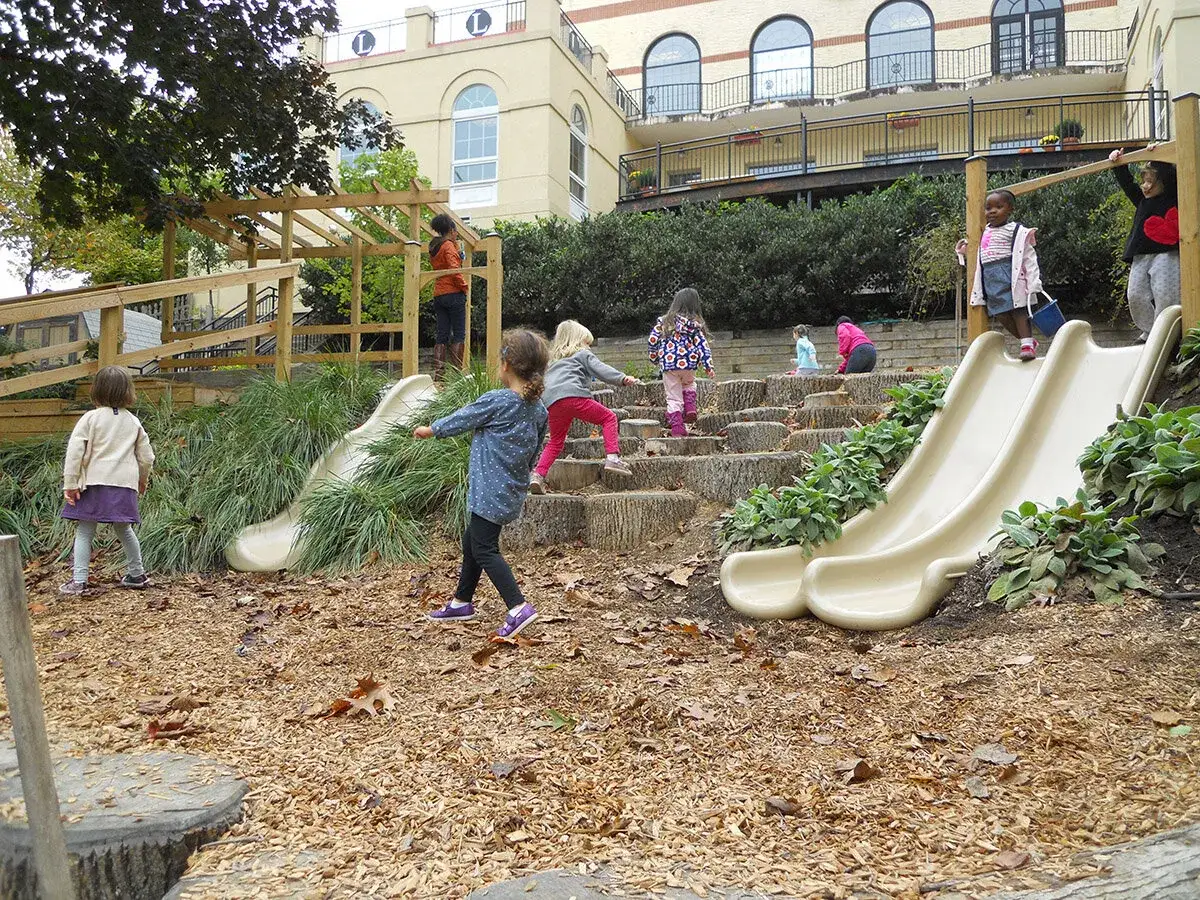 Kinder spielen fröhlich im Herbst im Kindergarten auf einer Rutsche und Holzstufen.