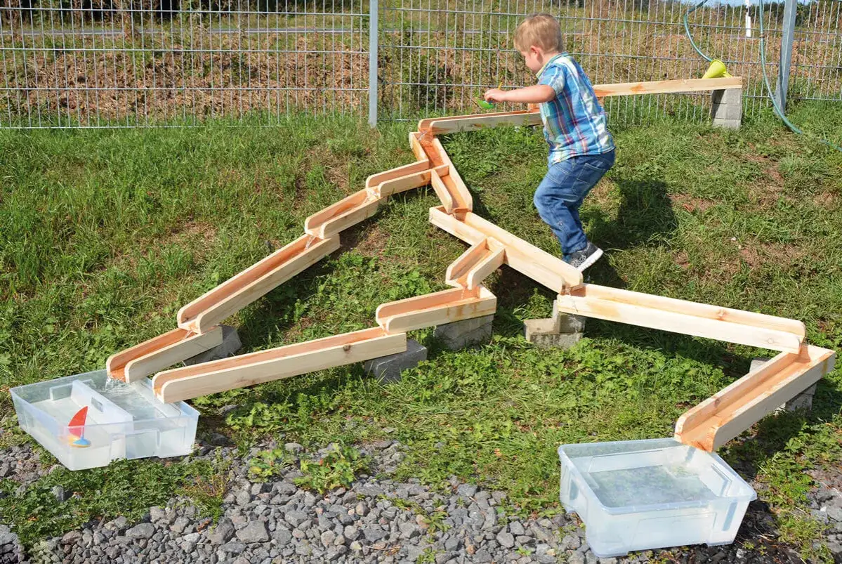 Kleiner Junge spielt mit einer Wasserrutsche im Garten. Tolle Kindergarten spiele f&uuml;r drau&szlig;en.