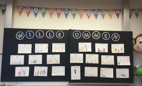 Willkommen zur 1. Klasse! Kinderzeichnungen schmücken die Tafel, ein bunter ABC-Girlande hängt darüber.