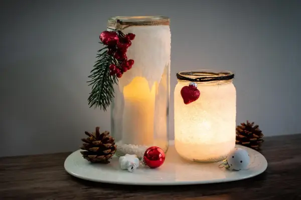 Zwei selbstgebastelte Windlichter mit Salz, Kerzen und weihnachtlichem Schmuck. Ein DIY-Projekt, das Gemütlichkeit bringt.